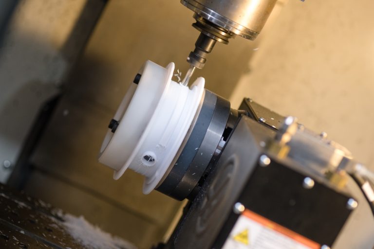 CNC-freesmachine die een wit kunststof onderdeel bewerkt